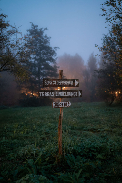 Letrero de madera en un campo verde con niebla en el parque vacacional RØSTIG Dorst en Brabante Septentrional.
