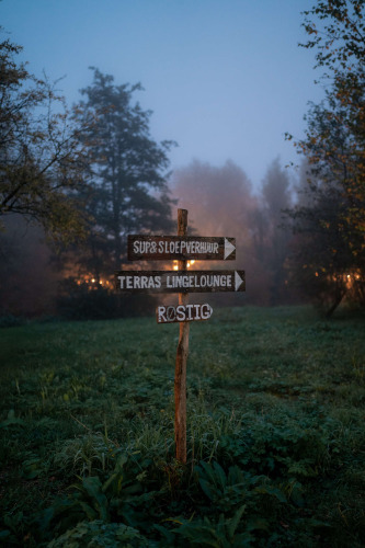 Wooden signpost in a misty green field at RØSTIG Dorst holiday park in North Brabant, Netherlands at dusk.