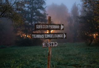 Holzschild auf einer Wiese im Nebel bei RØSTIG Dorst Ferienpark in Nordbrabant, Niederlande, am Abend.