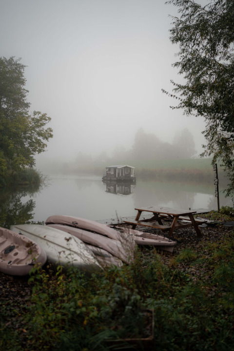 Nebliger Morgen im Ferienpark RØSTIG Dorst, Niederlande, mit Booten im Vordergrund, Hausboot auf See.