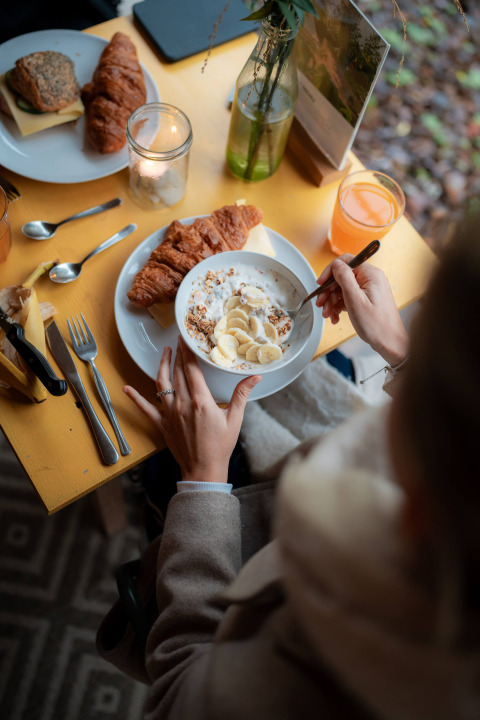Desayuno con croissant, yogur con plátano y granola en mesa amarilla en el parque RØSTIG Dorst.