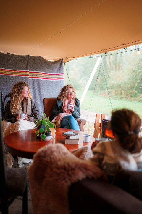 Drei Frauen entspannen mit heißen Getränken und Decken in einer gemütlichen Ferienanlage in Nordbrabant.