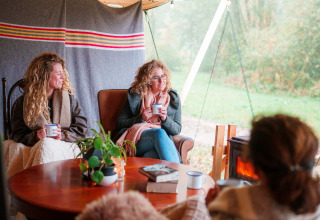 Tre donne si rilassano con bevande calde e coperte a RØSTIG Dorst, parco vacanze in Noord-Brabant.