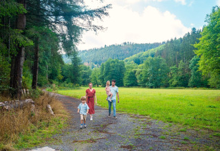 Gezin wandelt op een bospad met groene heuvels op de achtergrond bij hun glamping accommodatie.