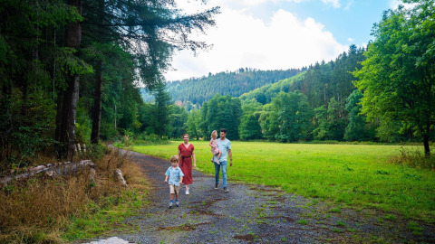 Gezin maakt een wandeling op een bosweg aan hun glamping accommodatie met groene heuvels rondom.