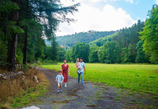 Gezin maakt een wandeling op een bosweg aan hun glamping accommodatie met groene heuvels rondom.