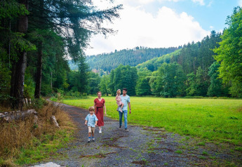 Familie går en tur på en skovsti med grønne bakker bagved, nær deres glamping overnatning.