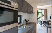 Modern kitchen and dining area at Cube La Mer, Kohnenhof Luxembourg, featuring sleek gray cabinetry and natural light.