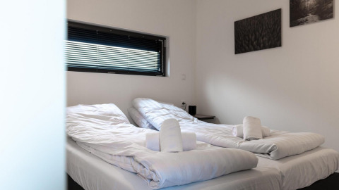 Moderne tweepersoonskamer in Cube La Mer te Kohnenhof, Luxemburg met witte bedden en opgerolde handdoeken.