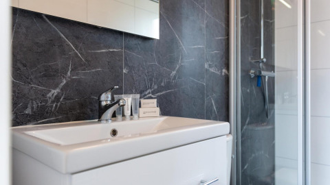 Baño moderno en Cube La Mer, Kohnenhof, Luxemburgo con lavabo, paredes de mármol oscuro y ducha.