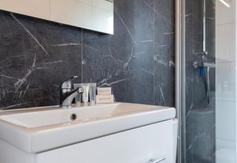 Modernes Badezimmer im Cube La Mer, Kohnenhof, Luxemburg mit Waschbecken, dunklen Wänden und Dusche.