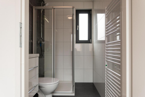 Moderne badkamer met douche, toilet, venster en betegelde muren in Cube La Mer op Kohnenhof, Luxemburg.