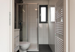 Moderne badkamer met douche, toilet, venster en betegelde muren in Cube La Mer op Kohnenhof, Luxemburg.