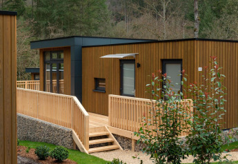 Moderne Holzlodge mit Rampe und Terrasse bei Cube La Mer in Kohnenhof, Luxemburg, von Bäumen umgeben.