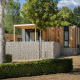 Moderne Domus lodge med træfacade, stenmur og terrasse i naturskønt område med grøn beplantning.
