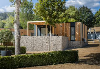 Moderne Domus lodge met houten gevel, stenen muur en terras in een groene, natuurlijke omgeving.