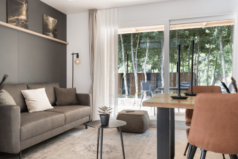 Modern living room at Domus lodge in Kohnenhof, Luxembourg, with forest view through large windows.