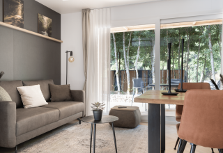 Modern living room at Domus lodge in Kohnenhof, Luxembourg, with forest view through large windows.
