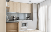 Modern kitchenette at Domus at Kohnenhof in Luxembourg with wooden cabinets, appliances, and large window.