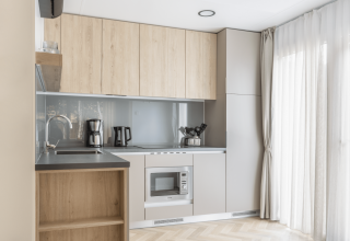 Modern kitchenette at Domus at Kohnenhof in Luxembourg with wooden cabinets, appliances, and large window.