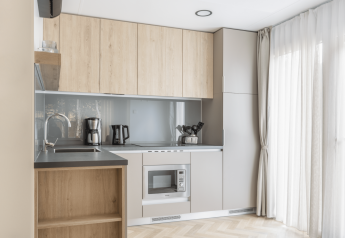 Modern kitchenette bij Domus aan Kohnenhof in Luxemburg met houten kasten en groot raam met gordijnen.