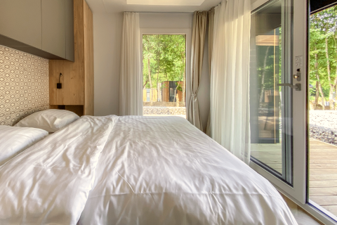 Modern bedroom with large windows and white bedding at Domus lodge, Kohnenhof, Luxembourg, wooded view.