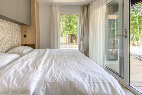 Modern bedroom with large windows and white bedding at Domus lodge, Kohnenhof, Luxembourg, wooded view.
