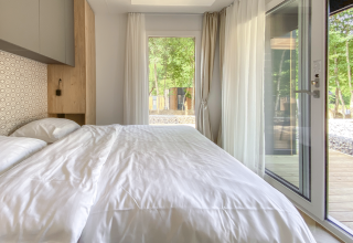 Modern bedroom with large windows and white bedding at Domus lodge, Kohnenhof, Luxembourg, wooded view.
