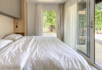 Modern slaapkamer met grote ramen, wit beddengoed en boszicht bij Domus lodge in Kohnenhof, Luxemburg.