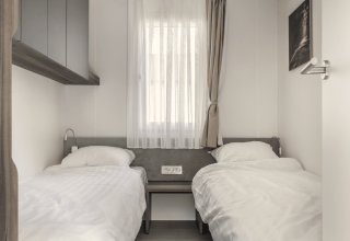 Een lichte kamer in een lodge met twee eenpersoonsbedden, witte lakens, raam met gordijnen en minimalistisch design.