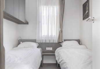 Een lichte kamer in een lodge met twee eenpersoonsbedden, witte lakens, raam met gordijnen en minimalistisch design.