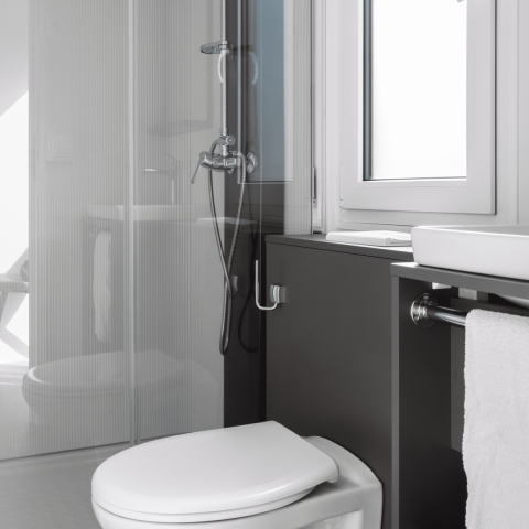 Baño moderno en una cabaña con inodoro, lavabo, ducha, ventana y toalla en un diseño minimalista.