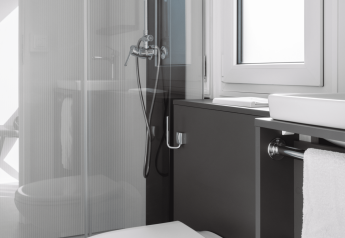 Moderne badeværelse på en lodge med toilet, håndvask, bruser, vindue og håndklæde i neutrale farver.