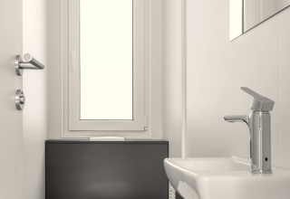 Modern, minimalistisch lodge-badkamer met toilet, wastafel en groot raam dat natuurlijk licht binnenlaat.