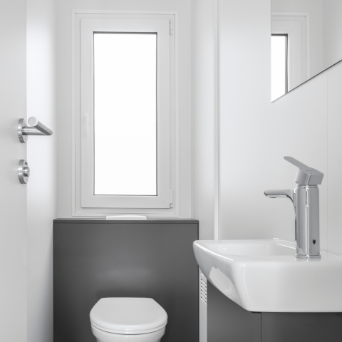Baño moderno y minimalista en una cabaña, con inodoro, lavabo y una ventana grande para luz natural.
