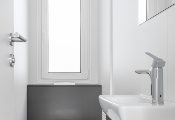 Salle de bains moderne et minimaliste dans un lodge, avec toilettes, lavabo et une grande fenêtre lumineuse.