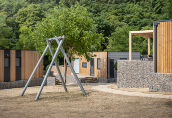 Buitenaanzicht van Domus lodge met moderne houten huisjes, stenen hekken, schommel en veel groen.