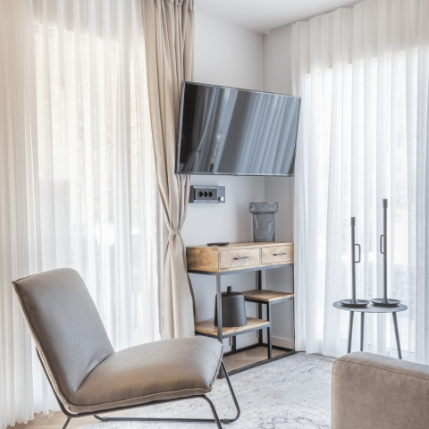 Salon moderne du lodge Domus à Kohnenhof, Luxembourg, avec fauteuil, TV murale et lumière naturelle.