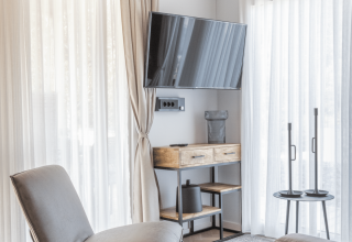 Salon moderne du lodge Domus à Kohnenhof, Luxembourg, avec fauteuil, TV murale et lumière naturelle.