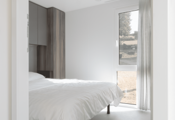 Chambre claire et moderne d’un lodge avec grand lit blanc, fenêtre panoramique et placard en bois.