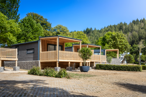 Moderne Silvanus lodge met houten terras, gelegen tussen groen en bos onder een heldere blauwe lucht.