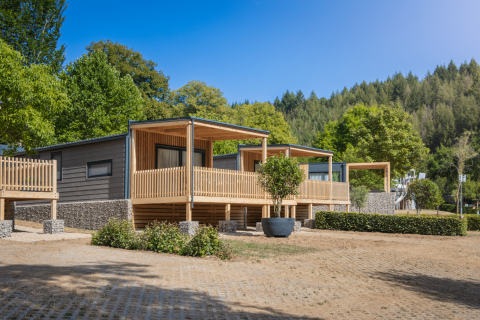 Lodge Silvanus moderno con terraza de madera, rodeado de vegetación y bosque bajo un cielo azul claro.