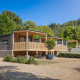 Moderne trælodge Silvanus med store terrasser, omgivet af grønt område og skov under blå himmel.