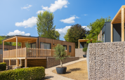 Modern Silvanus lodges at Kohnenhof, Luxembourg, with stone walls and greenery under blue sky.