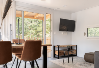 Lichte woonruimte in Silvanus-lodge te Kohnenhof, Luxemburg, met eettafel, tv en uitzicht op bos.
