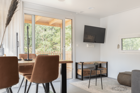 Sala luminosa en la cabaña Silvanus en Kohnenhof, Luxemburgo, con mesa de comedor, TV y vista al bosque.