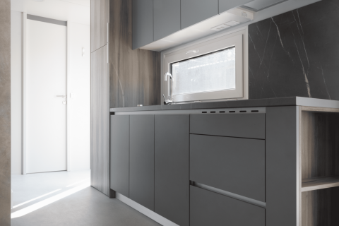 Cocina moderna minimalista en la cabaña Silvanus en Kohnenhof, Luxemburgo, con muebles grises y ventana.