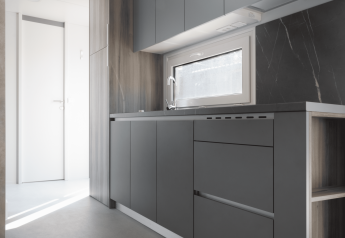Moderne, minimalistisk køkken i Silvanus-lodgen ved Kohnenhof i Luxembourg med grå skabe og vindue.