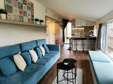 Moderne stue og køkken i Panorama Cottage på Gulperberg, Nederlandene, med blå sofaer og lyse træmøbler.
