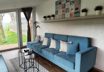 Soggiorno moderno al Panorama Cottage di Gulperberg, Paesi Bassi, con divano blu e grandi vetrate.